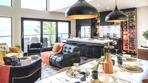 Una sala de estar moderna con un ventanal grande, un comedor con mesa dispuesta para seis personas y una cocina con estante para vinos.