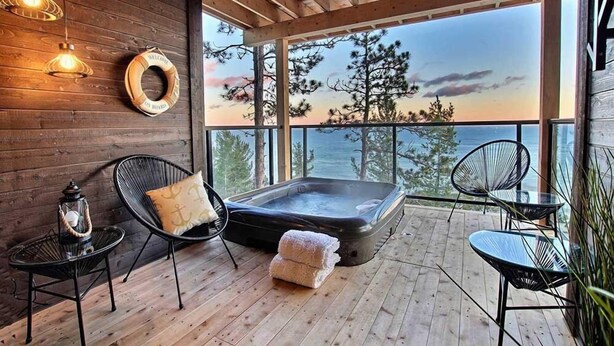 Una terraza de madera con un jacuzzi, sillas de descanso y vista al océano.