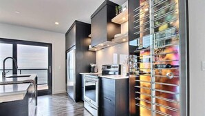 Una cocina moderna con armarios oscuros, electrodomésticos de acero inoxidable y una vinera con puertas de vidrio.