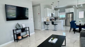 Une cuisine moderne avec des meubles blancs, un réfrigérateur en acier inoxydable et un coin repas avec des chaises bleues.