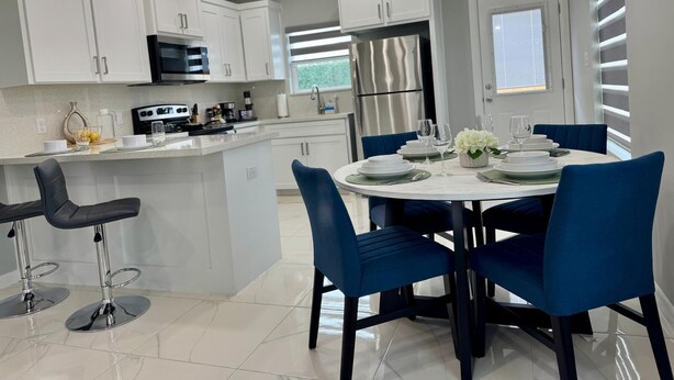 Une cuisine moderne avec des meubles blancs, un îlot central et des chaises bleues.