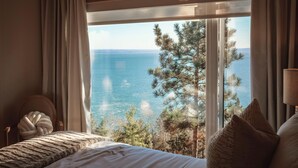 Een slaapkamer met een groot raam dat uitzicht biedt op de zee en bomen.