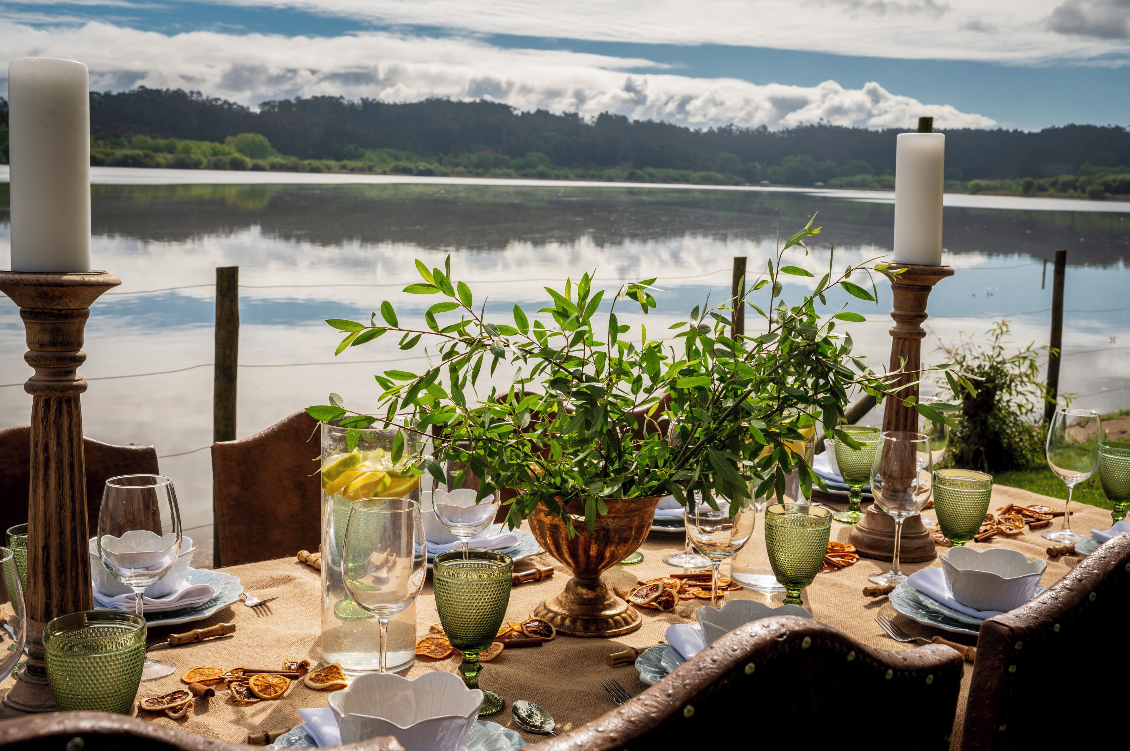 A lakeside dining table with candles, glassware, and a potted plant.