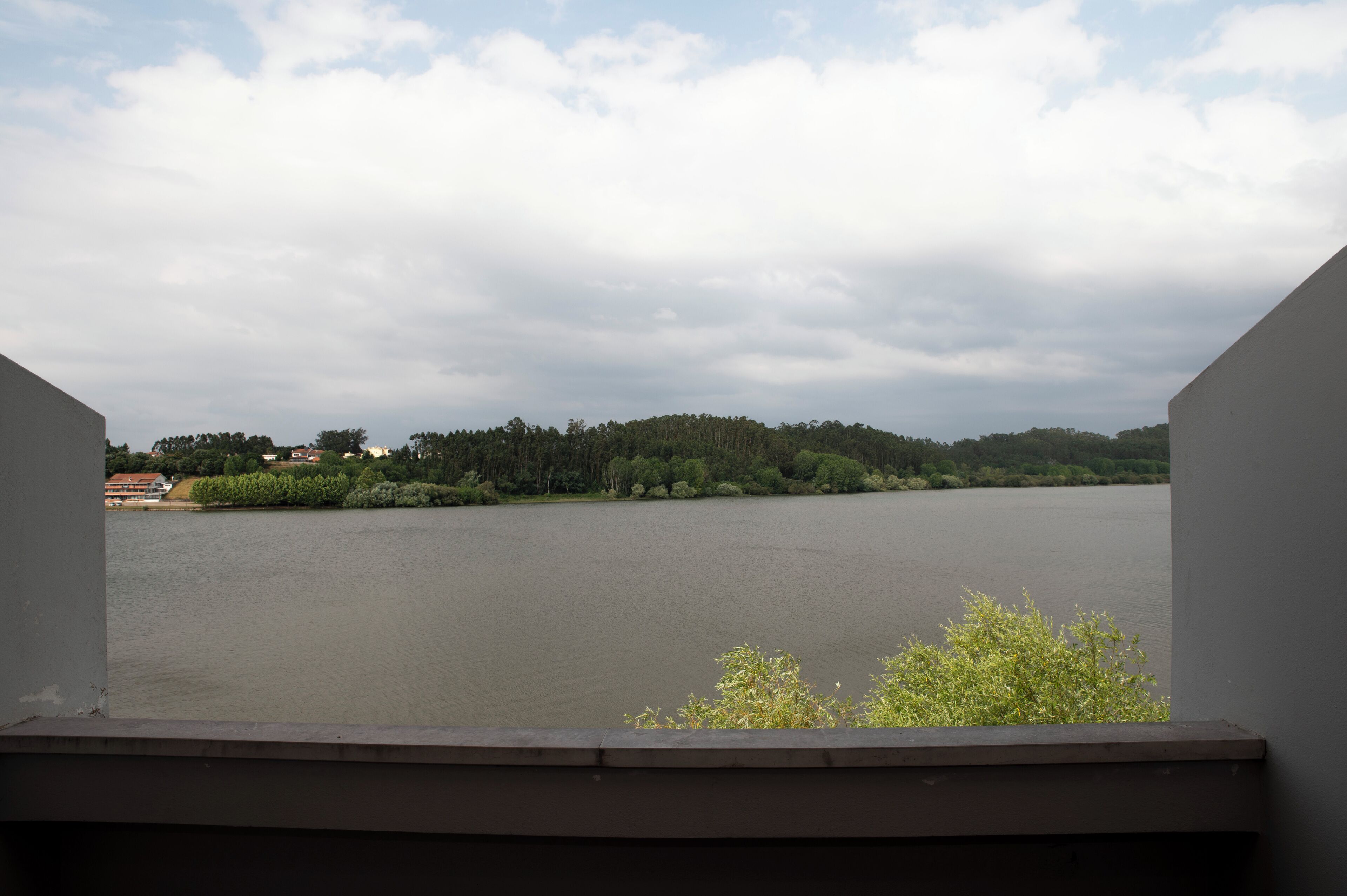Blick auf einen See von einem Balkon, im Hintergrund ein bewaldeter Hügel.