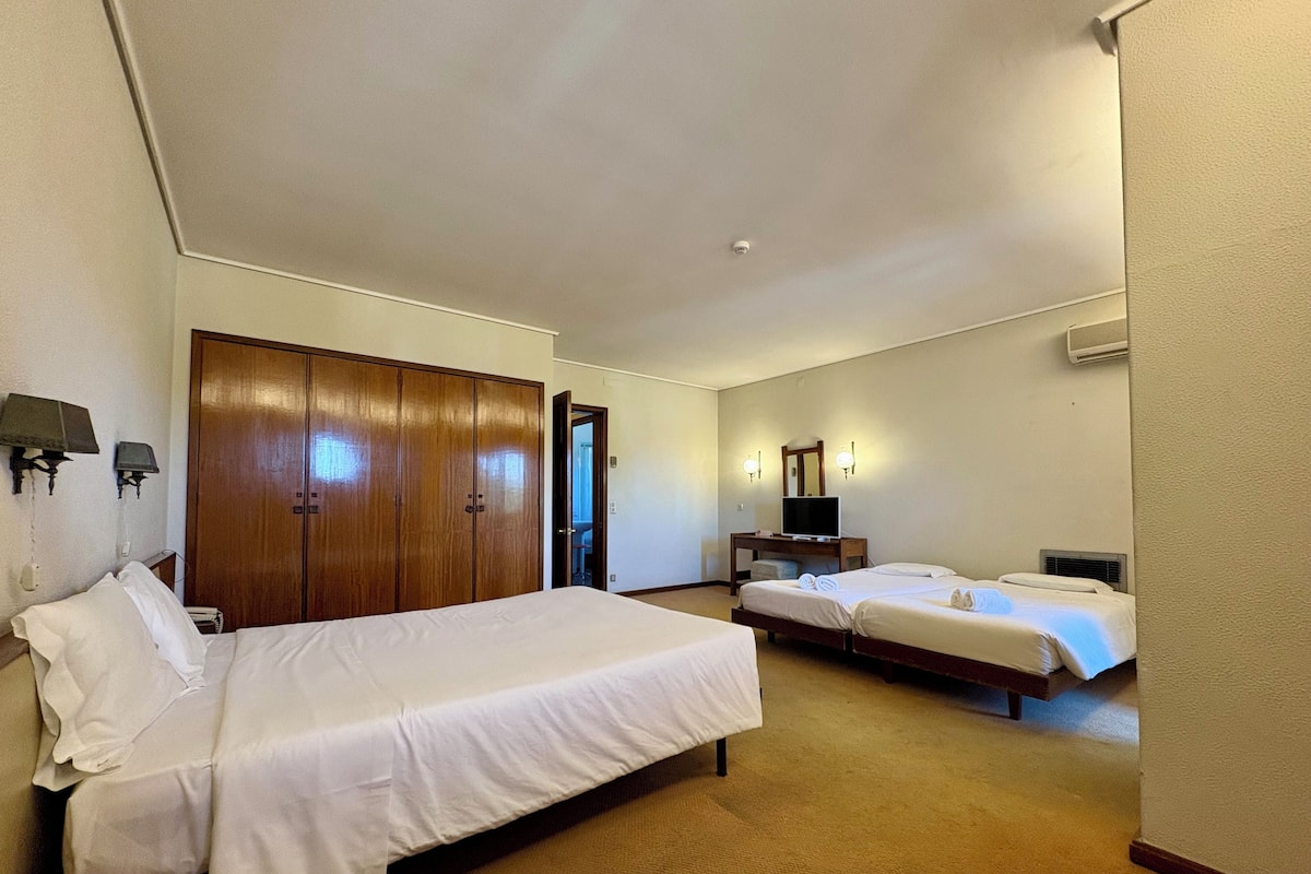 A hotel room with two beds, a wardrobe, a desk with a TV, and a bathroom visible through an open door.