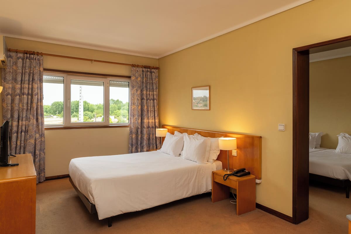 A hotel room with a large bed, bedside lamps, a desk with a telephone, and a window with curtains.