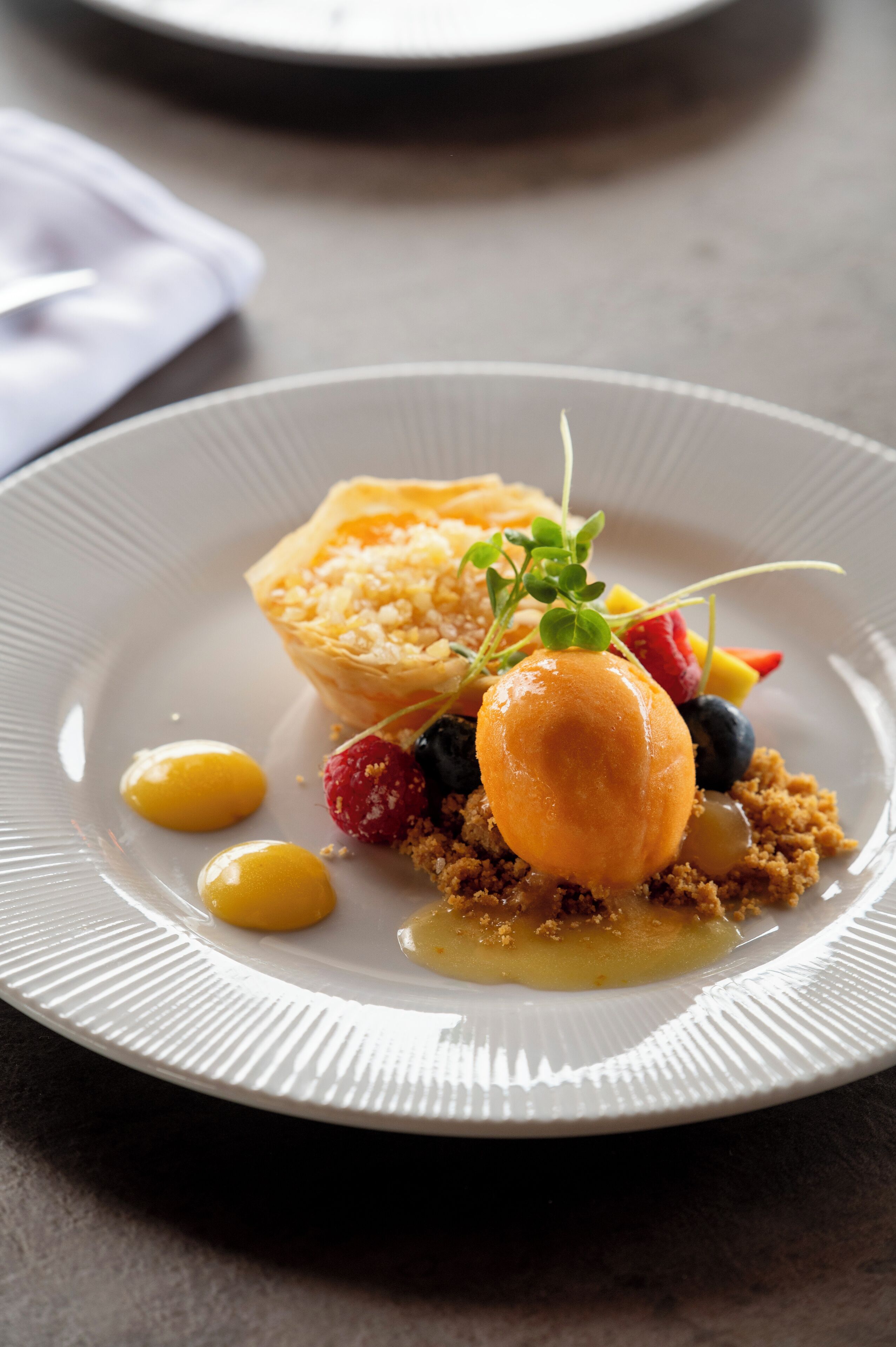 A dessert plate with a pastry, fruit, and a small green garnish.