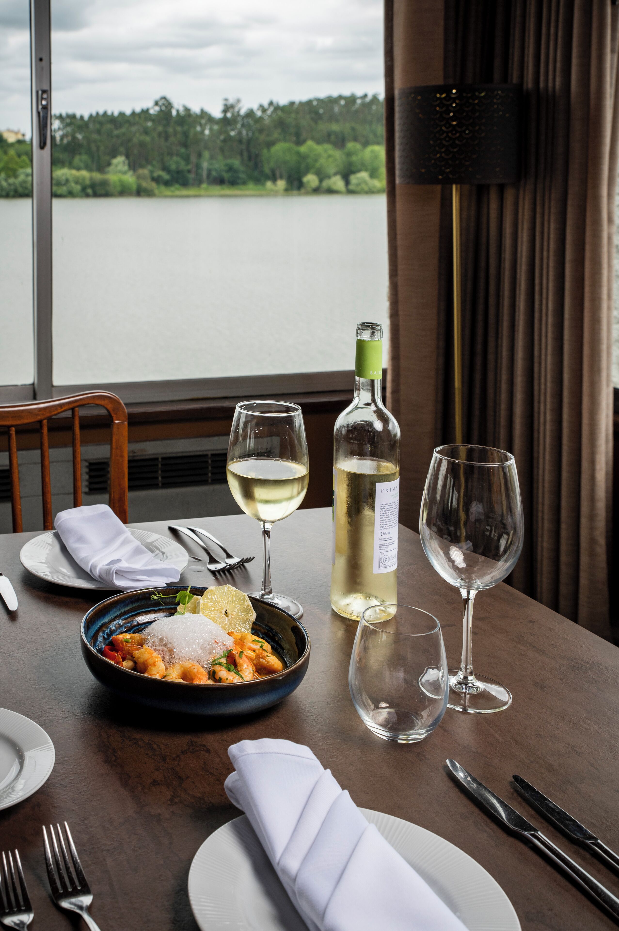 Une table à manger avec une bouteille de vin blanc, deux verres à vin, un plat de pâtes et des couverts disposés avec soin.