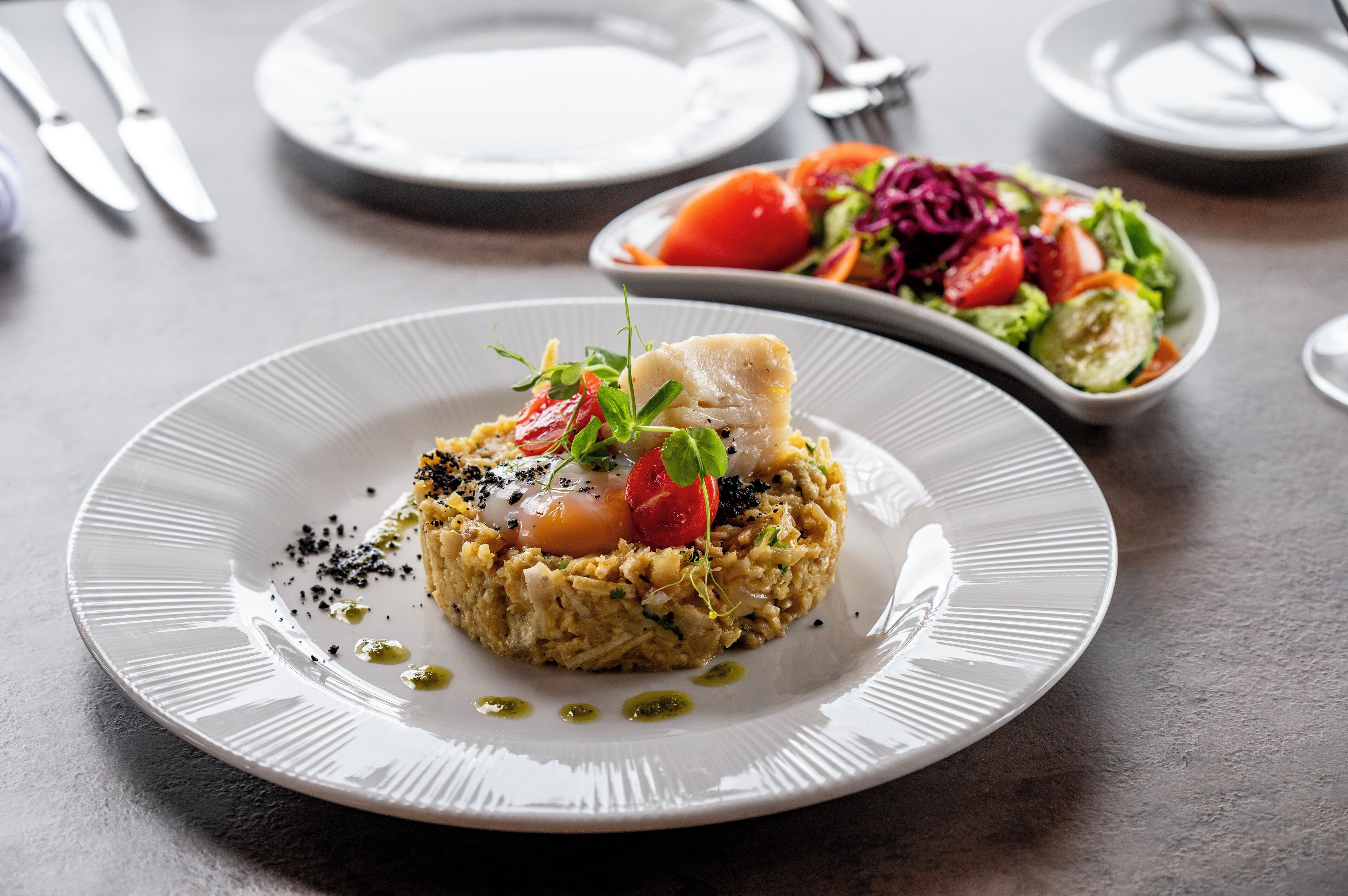 Ein Teller Essen mit Fisch, garniert mit Kräutern und einer Kirschtomate, auf einem weißen Teller.