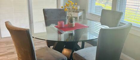 Un comedor con una mesa de vidrio, cuatro sillas, un jarrón con flores amarillas y un letrero que dice