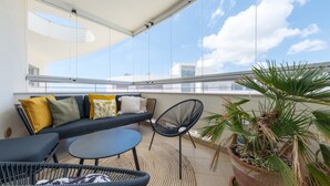 A balcony with a sofa, chairs, a small table, and a potted plant.