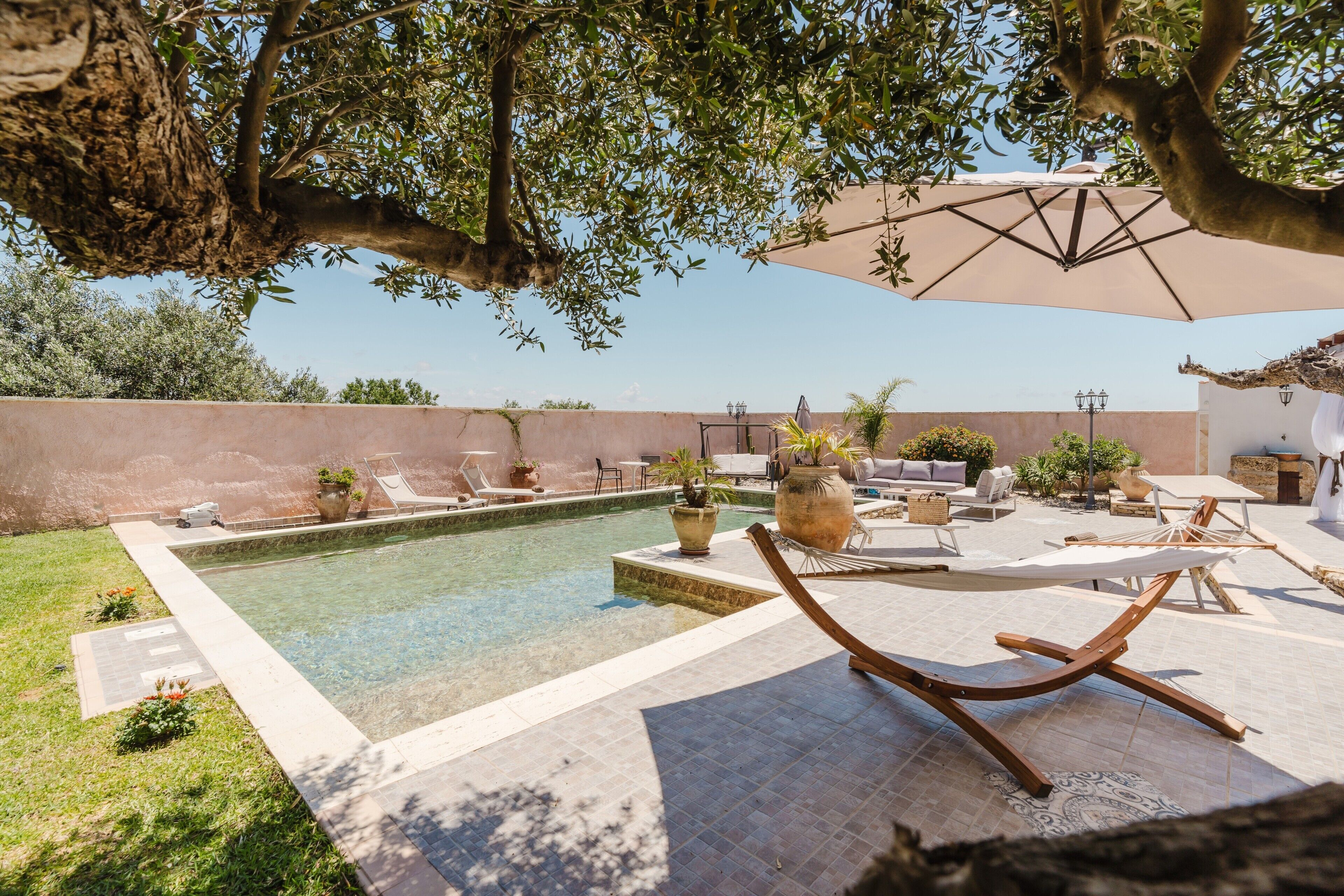 Ein Poolbereich mit Liegestühlen, einem Tisch und einem großen Sonnenschirm.