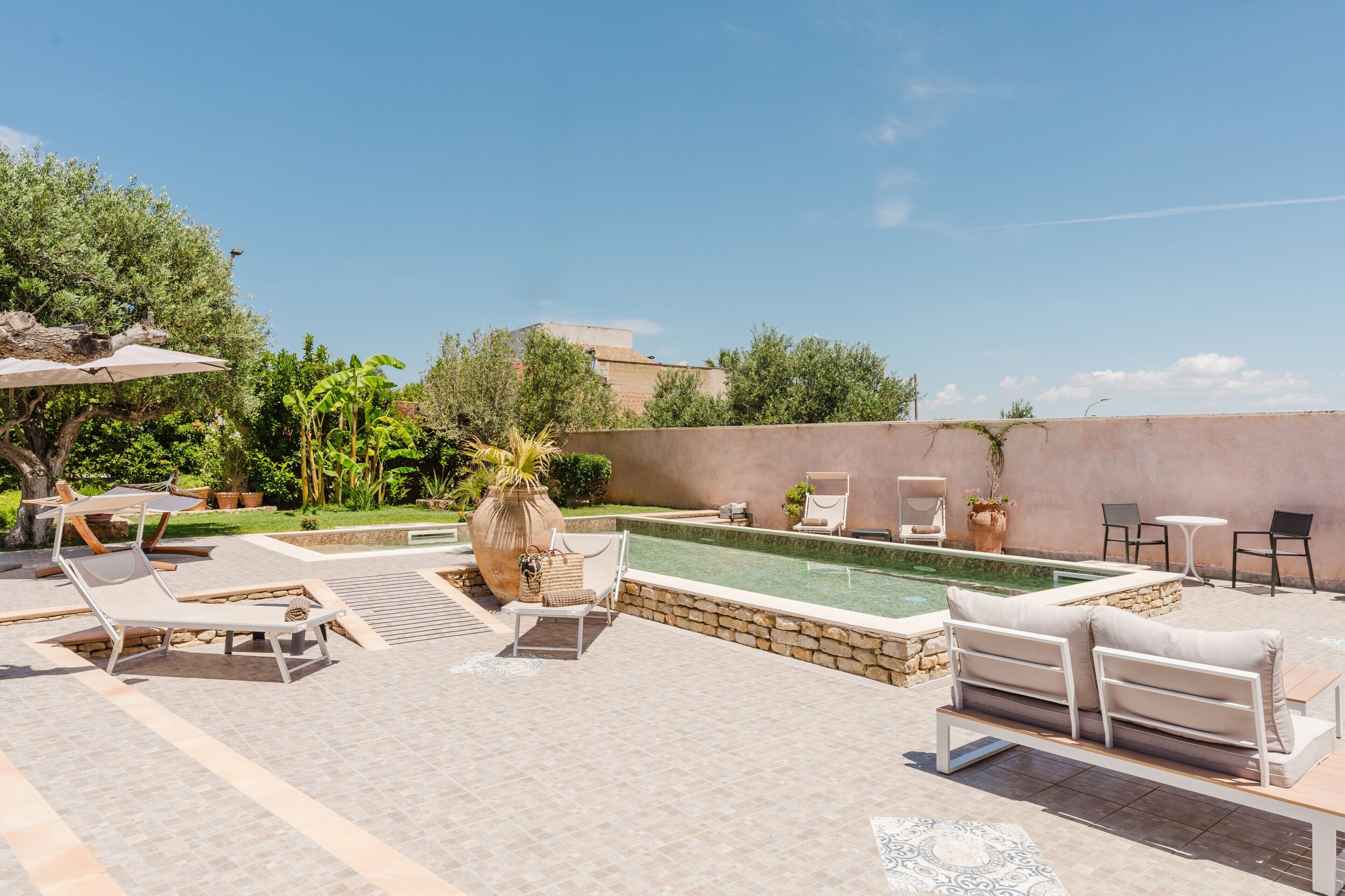 An outdoor pool area with lounge chairs, a table, and a potted plant.