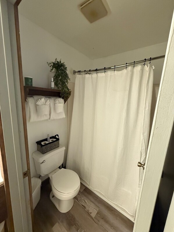 A small, compact bathroom with a toilet, a shelf with toiletries, and a shower curtain.