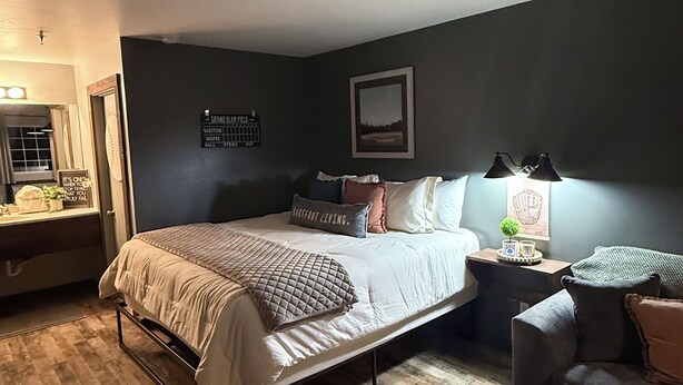 A bedroom with a bed, bedside tables, a chair, and a wall-mounted lamp. - 113 -The Sandlot- King Suite & Silver Dollar City Gem! (Branson)