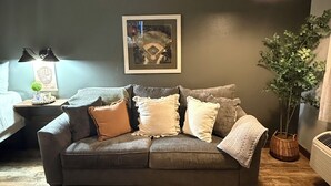 A living room with a grey couch, a framed picture on the wall, a hanging light fixture, and a potted plant. - 113 -The Sandlot- King Suite & Silver Dollar City Gem! (Branson)