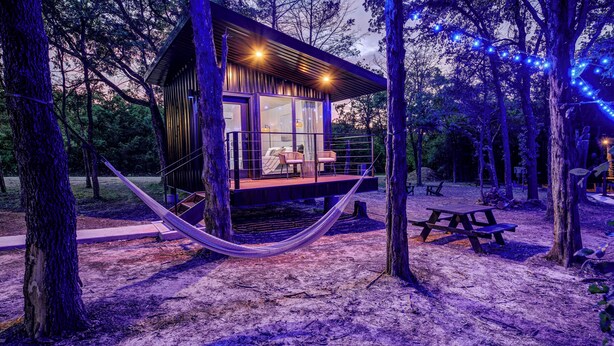 A modern cabin with a glass facade, wooden deck, and hammock. - Wooded Retreat w/ Pond View near LBJ Grasslands - 4 Cabins/Sleeps 8 (Alvord)