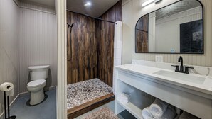 Ein modernes Badezimmer mit einer Duschkabine aus Holz, einer weißen Toilette und einem Waschtisch mit großem Spiegel.