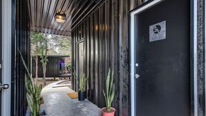 A modern building entrance with a metal exterior, a black door, and potted plants. - Wooded Retreat w/ Pond View near LBJ Grasslands - 4 Cabins/Sleeps 8 (Alvord)