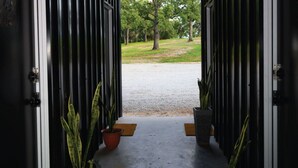 An open doorway leading to a gravel path with potted plants on either side. - Wooded Retreat w/ Pond View near LBJ Grasslands - 4 Cabins/Sleeps 8 (Alvord)