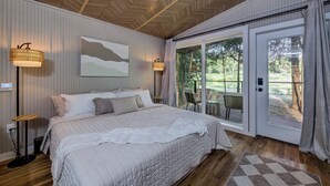 A bedroom with a large bed, a view of the outdoors through a sliding glass door, and a ceiling with a herringbone pattern. - Wooded Retreat w/ Pond View near LBJ Grasslands - 4 Cabins/Sleeps 8 (Alvord)