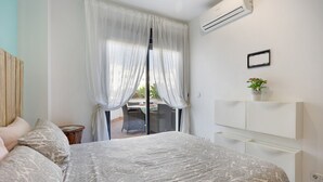 Un dormitorio con cama, mesita de noche, planta en maceta, puerta corredera de vidrio y aire acondicionado de pared.