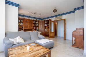 Uma sala de estar com um sofá cinza, estantes de madeira, uma mesa de centro de madeira e teto estampado.