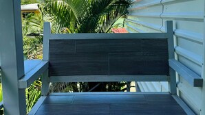 A wooden bench with a metal frame, positioned in front of a white building with horizontal siding. - Villas Cozy Sloth (Puerto Viejo de Talamanca)