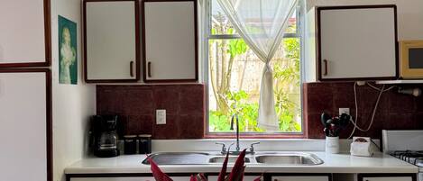A compact kitchen with white cabinets, a coffee machine, and a window with a view of greenery.