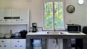 A modern kitchen with white cabinets, a large window, a sink, a coffee maker, and a microwave. - Villas Cozy Sloth (Puerto Viejo de Talamanca)