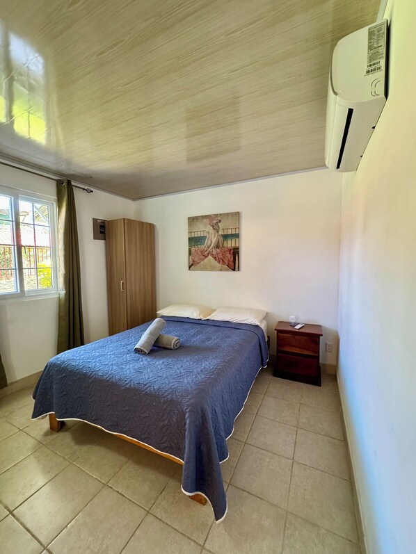 A bedroom with a bed, a nightstand, a wardrobe, a painting, and an air conditioning unit. - Villas Cozy Sloth (Puerto Viejo de Talamanca)
