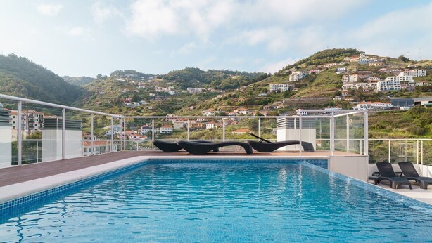 Une piscine dotée de chaises longues et offrant une vue sur une colline parsemée de bâtiments.