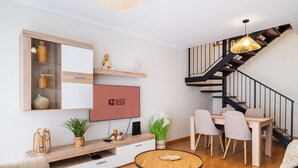 Un salon moderne doté d’un téléviseur à écran plat, de meubles en bois, d’un coin repas et d’un escalier avec une rampe noire.