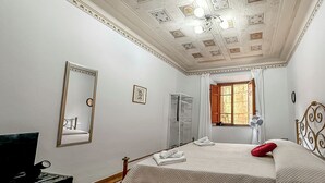 A hotel room with a bed, a mirror, a wardrobe, a window, and a ceiling with decorative elements. - Historical Apartment in the heart of Lucca (Lucca)