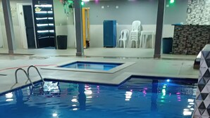 Piscina interior com superfície de água límpida, escada de metal e chão de azulejos.