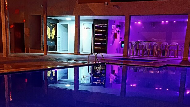 Piscina com escada de metal, rodeada por um edifício com iluminação roxa.