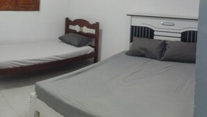 Quarto pequeno com duas camas de solteiro, um guarda-roupa de madeira e uma mesa de cabeceira branca.