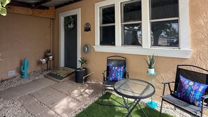 A covered patio with a table and chairs, a cactus decoration, and a door with a wreath.