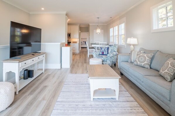 A modern living room with a flat-screen TV, a sofa, a coffee table, and a dining area with a table and chairs.