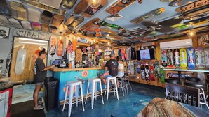 Een bar met een toonbank, krukken en een muur versierd met skateboards en andere voorwerpen.