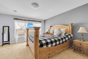 Une chambre à coucher avec un lit en bois, une table de chevet, une lampe et une fenêtre avec des rideaux.