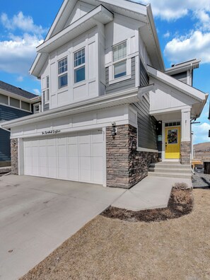 Une maison à deux étages avec un garage, des fondations en pierre et une porte d’entrée jaune.