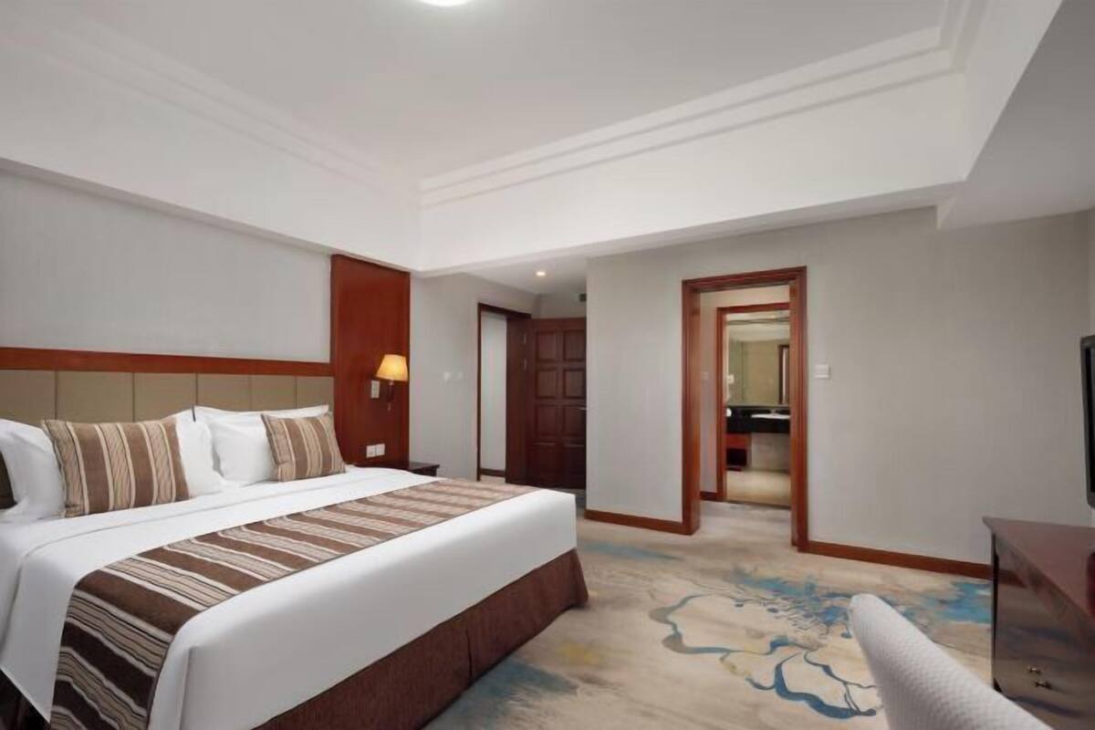 A hotel room with a large bed, a nightstand, a lamp, and a view of the hallway.