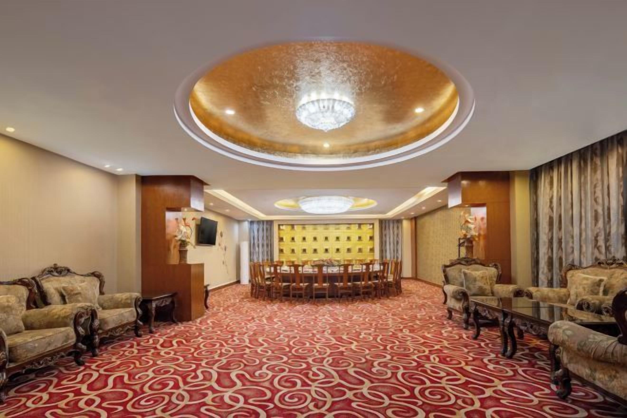 Un hall de hotel con alfombra roja estampada, un candelabro, una recepción y zonas de estar.