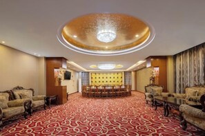 Un hall de hotel con alfombra roja estampada, un candelabro, una recepción y zonas de estar.