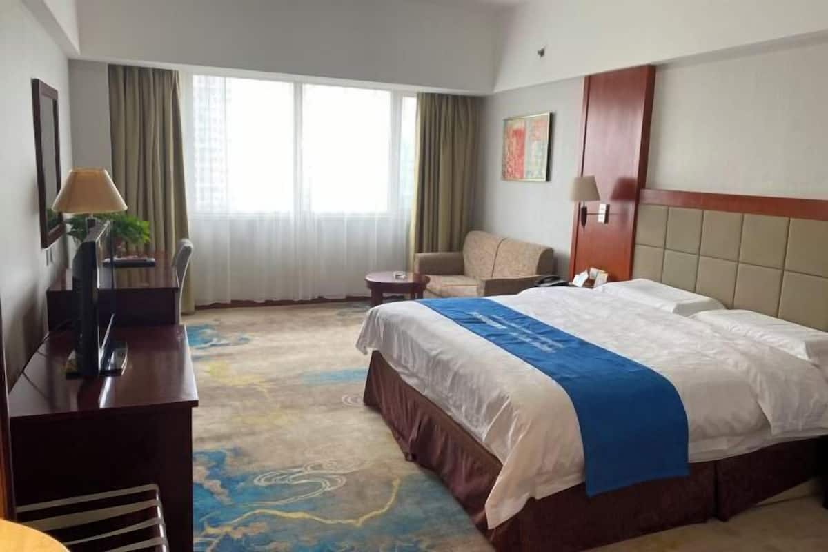 A hotel room with a large bed, a desk with a lamp, a chair, and a small table.