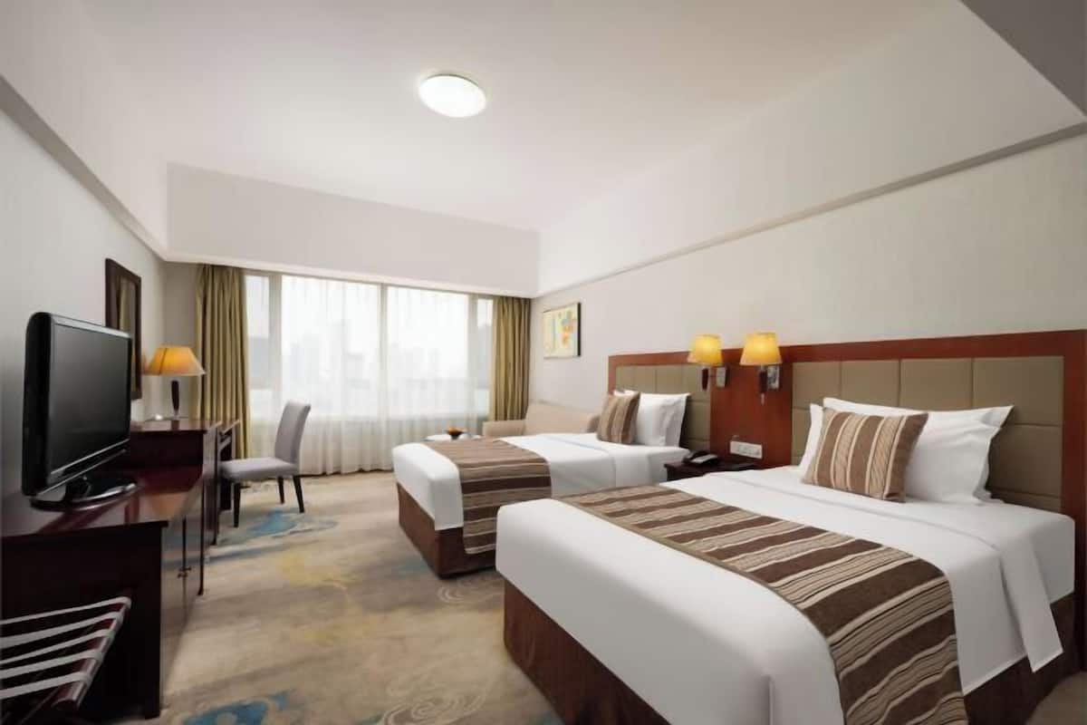 A hotel room with two beds, a TV, a desk, and a window with curtains.
