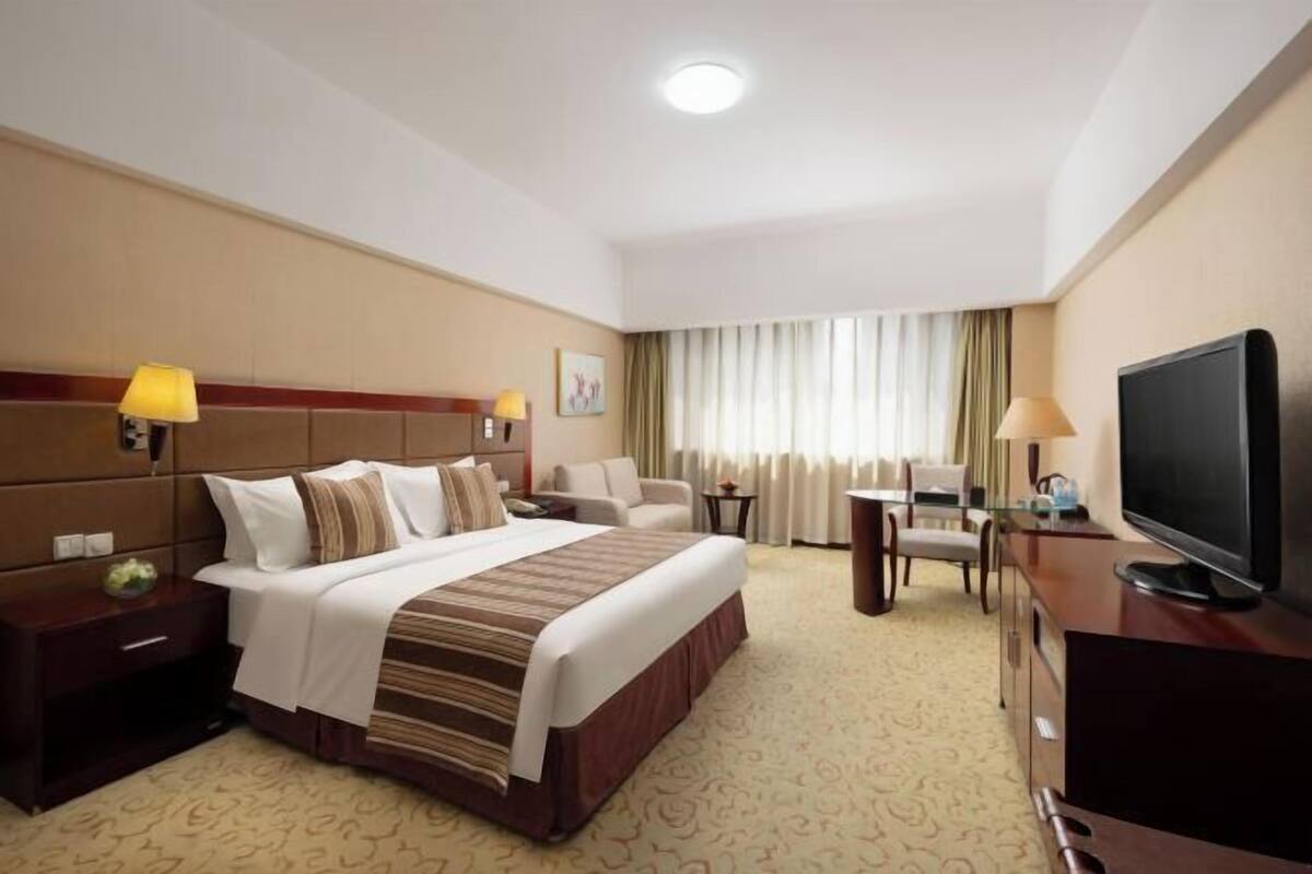 A hotel room with a bed, bedside tables, a TV, a desk, and a chair.