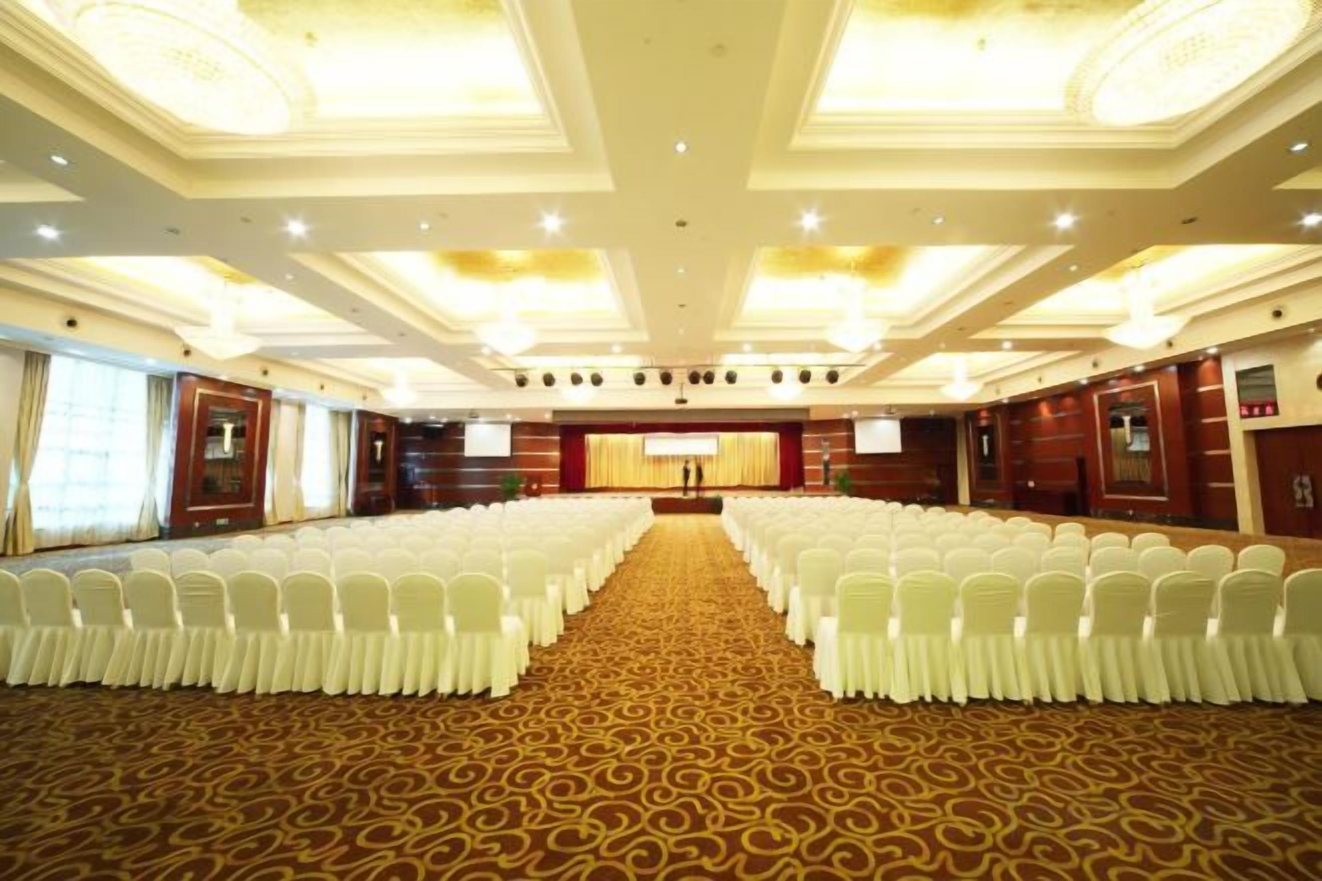 A conference room with rows of white chairs, a carpeted floor, and a stage with a podium.
