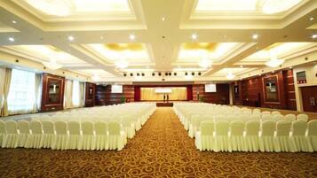 A conference room with rows of white chairs, a carpeted floor, and a stage with a podium.